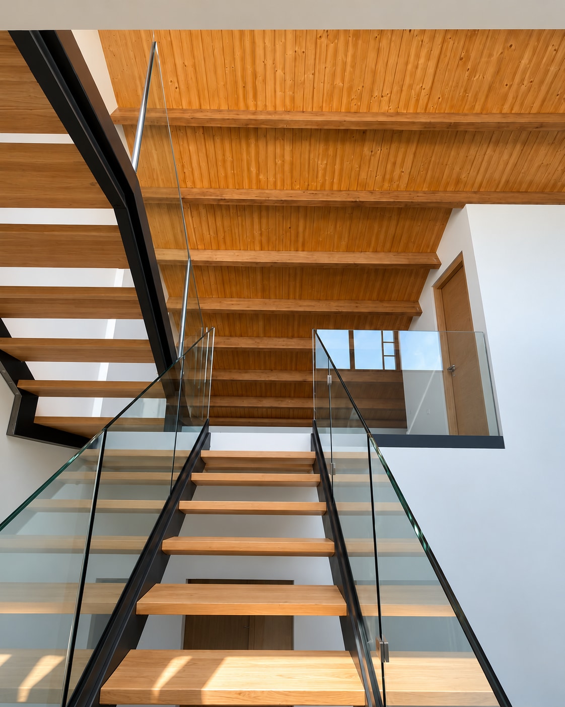 Wooden open-tread staircase with glass balustrade in a home renovation in Teulada